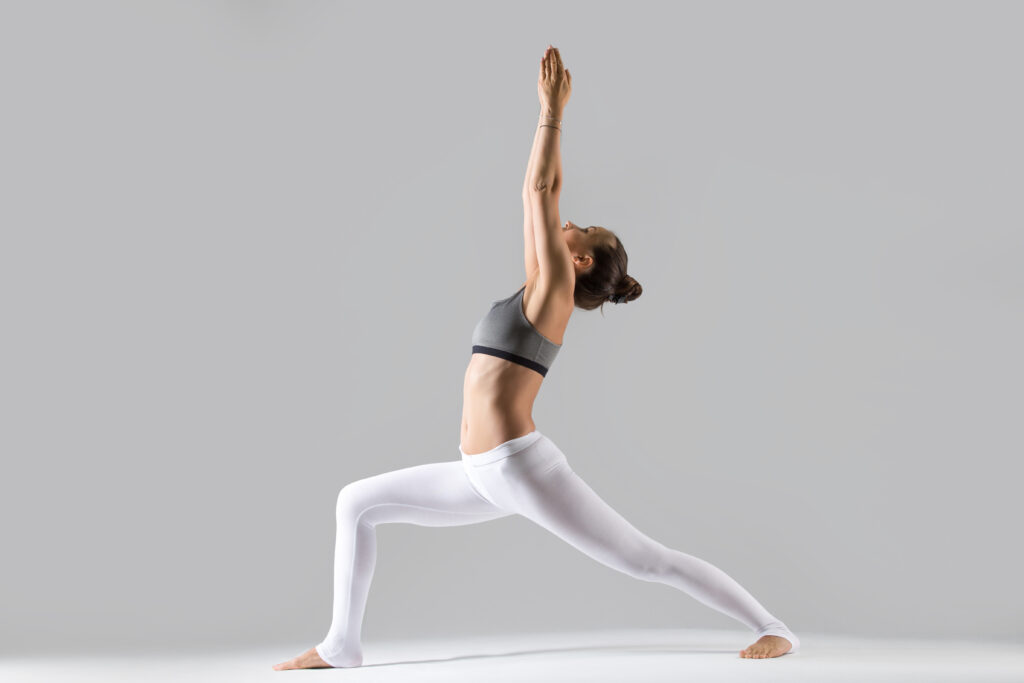 young woman virabhadrasana i pose grey studio background